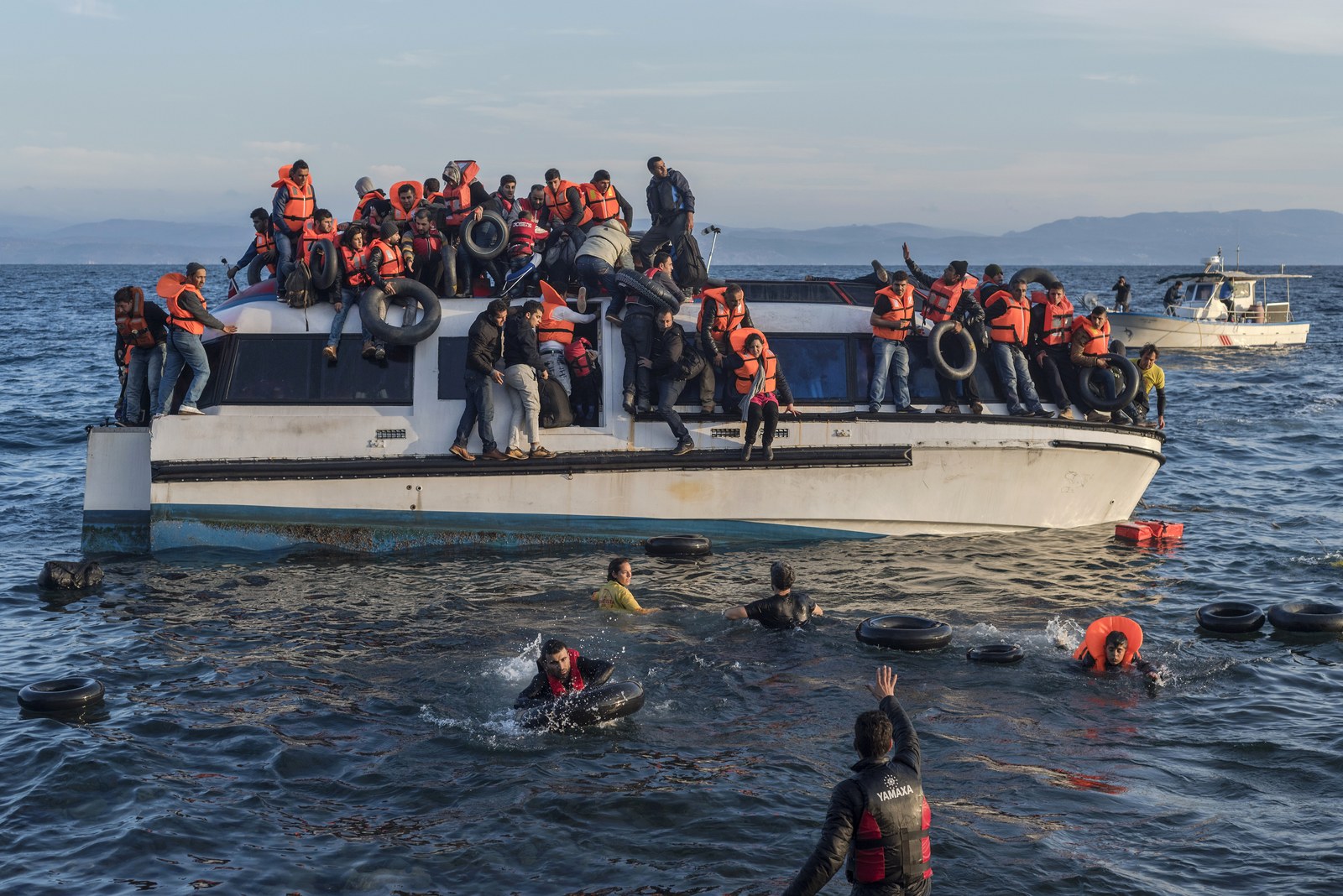 Migrant boats and a ferry on the Aegean Sea off Lesvos at dusk, near where smugglers run the crossing from Turkey