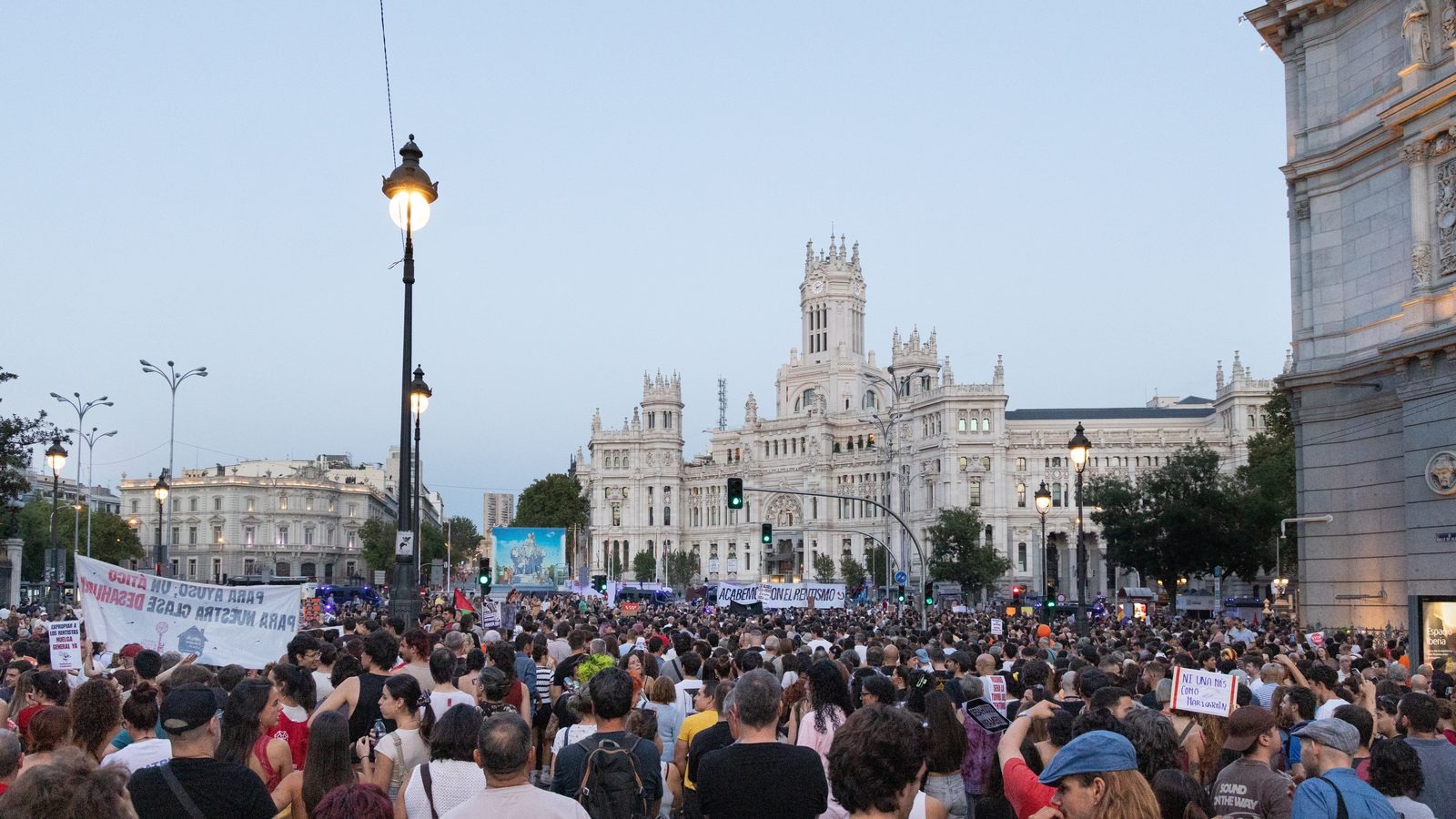 Demonstrators marching through a city street carrying flags and signs at a daytime protest